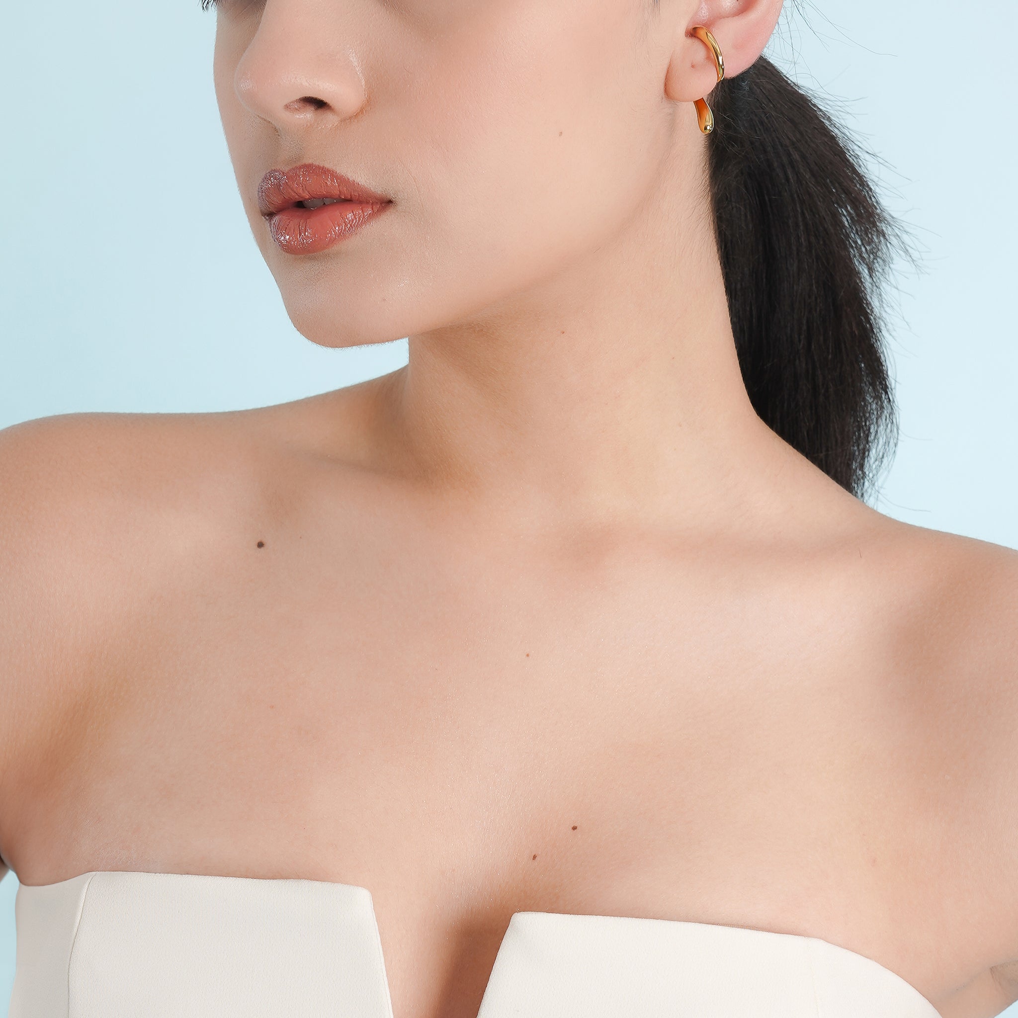 Woman wearing an 18K gold-plated abstract swirl earring with a sleek, curved design that wraps around the ear for a minimalist, elegant look.