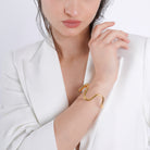 A model wearing an 18K gold-plated abstract bracelet with an organic, wavy design, styled elegantly against a minimalist white outfit.