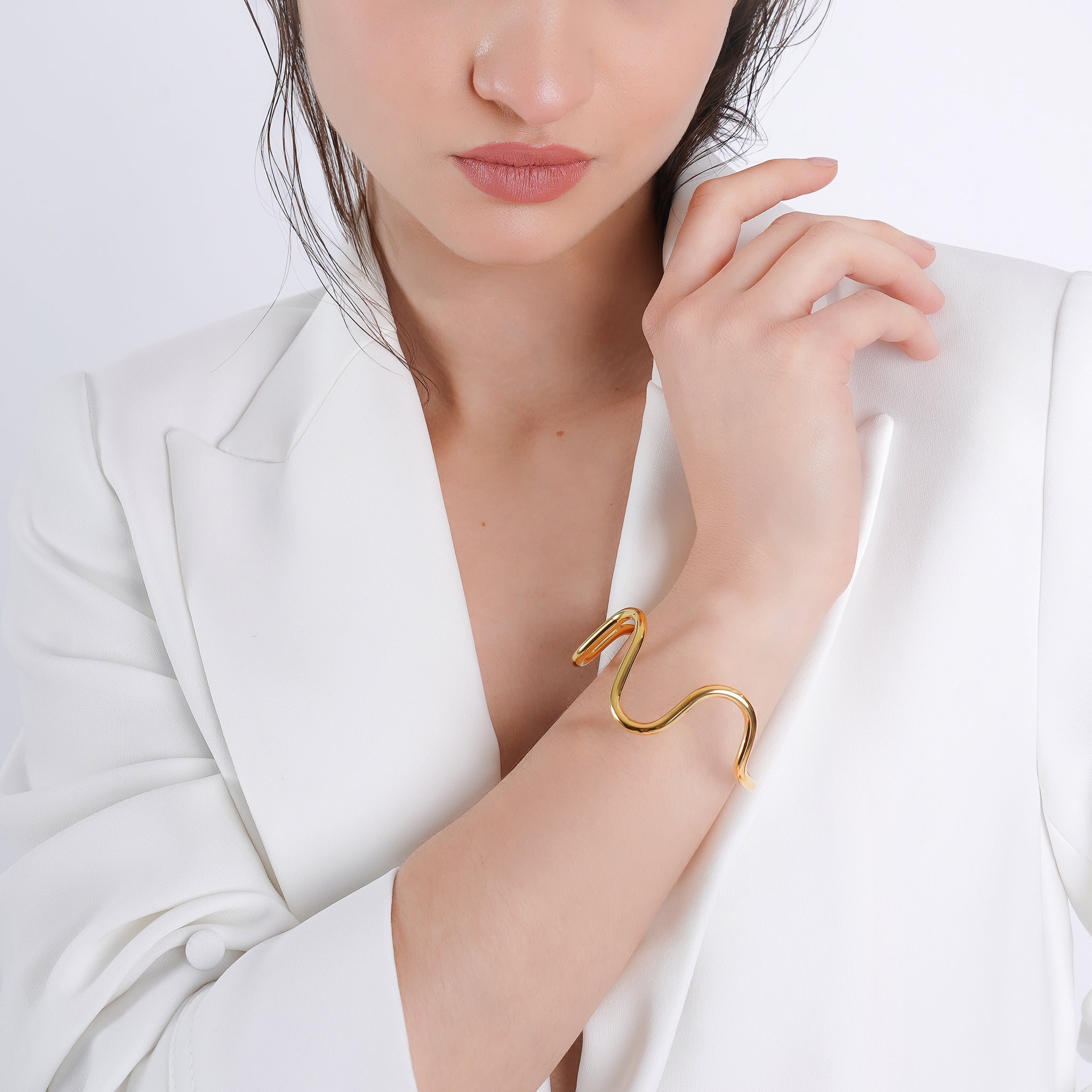 A model wearing an 18K gold-plated abstract bracelet with an organic, wavy design, styled elegantly against a minimalist white outfit.