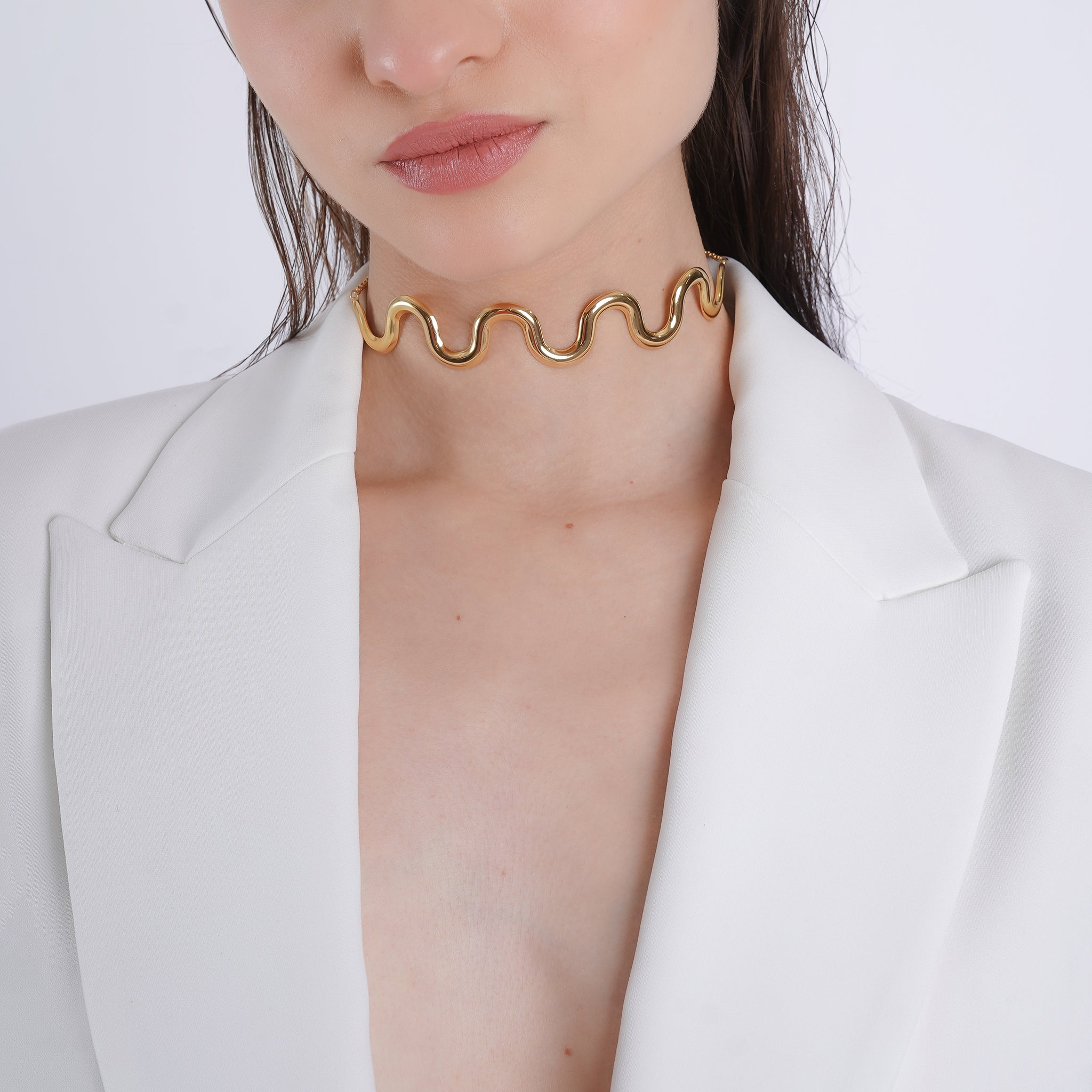 A model wearing the wavy, gold-tone choker against a white blazer, highlighting the necklace’s sleek, bold curves and its modern, sophisticated appeal.