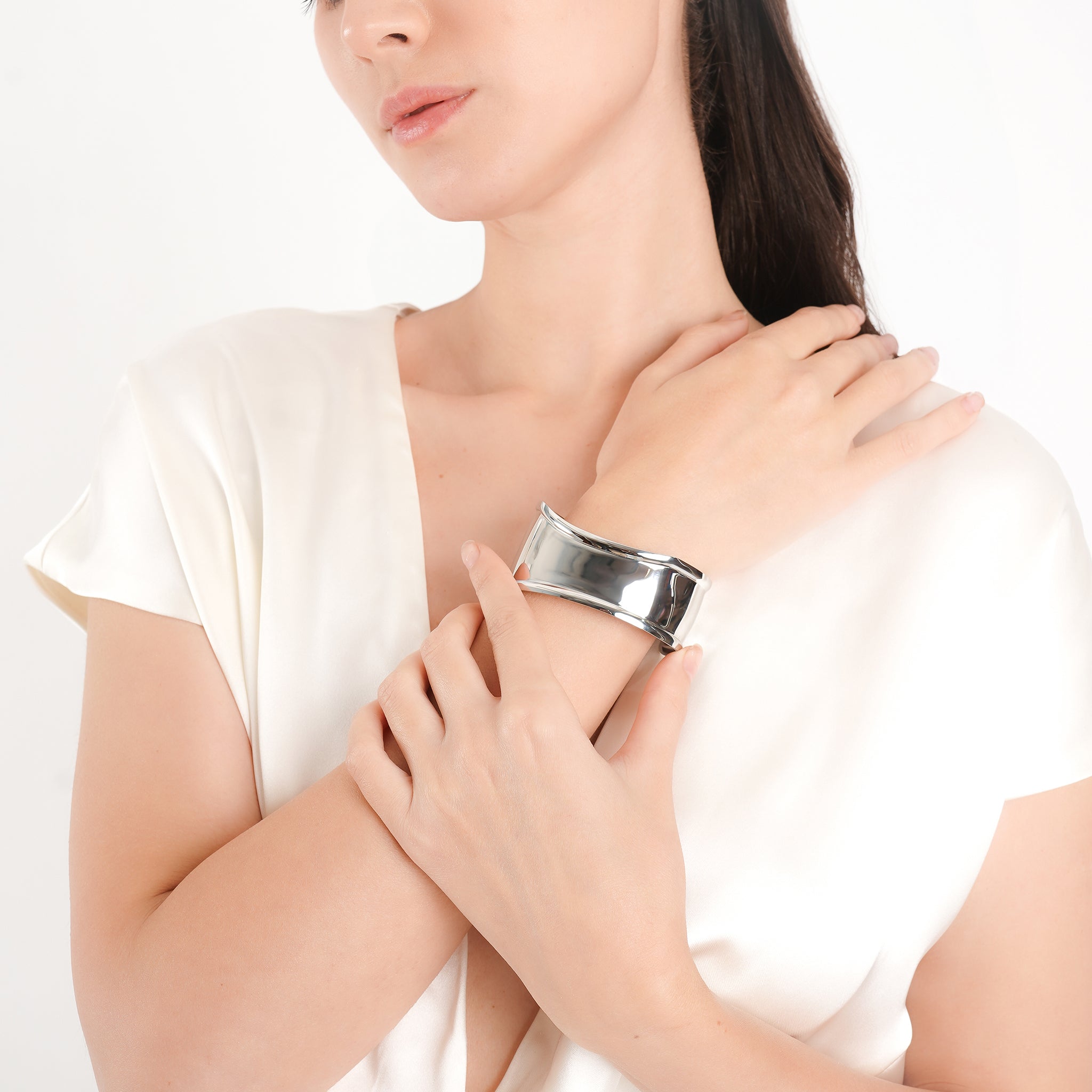 A model wearing the silver polished cuff bracelet on her wrist, paired with a strapless, minimalist white outfit, highlighting the bracelet's bold, reflective design.