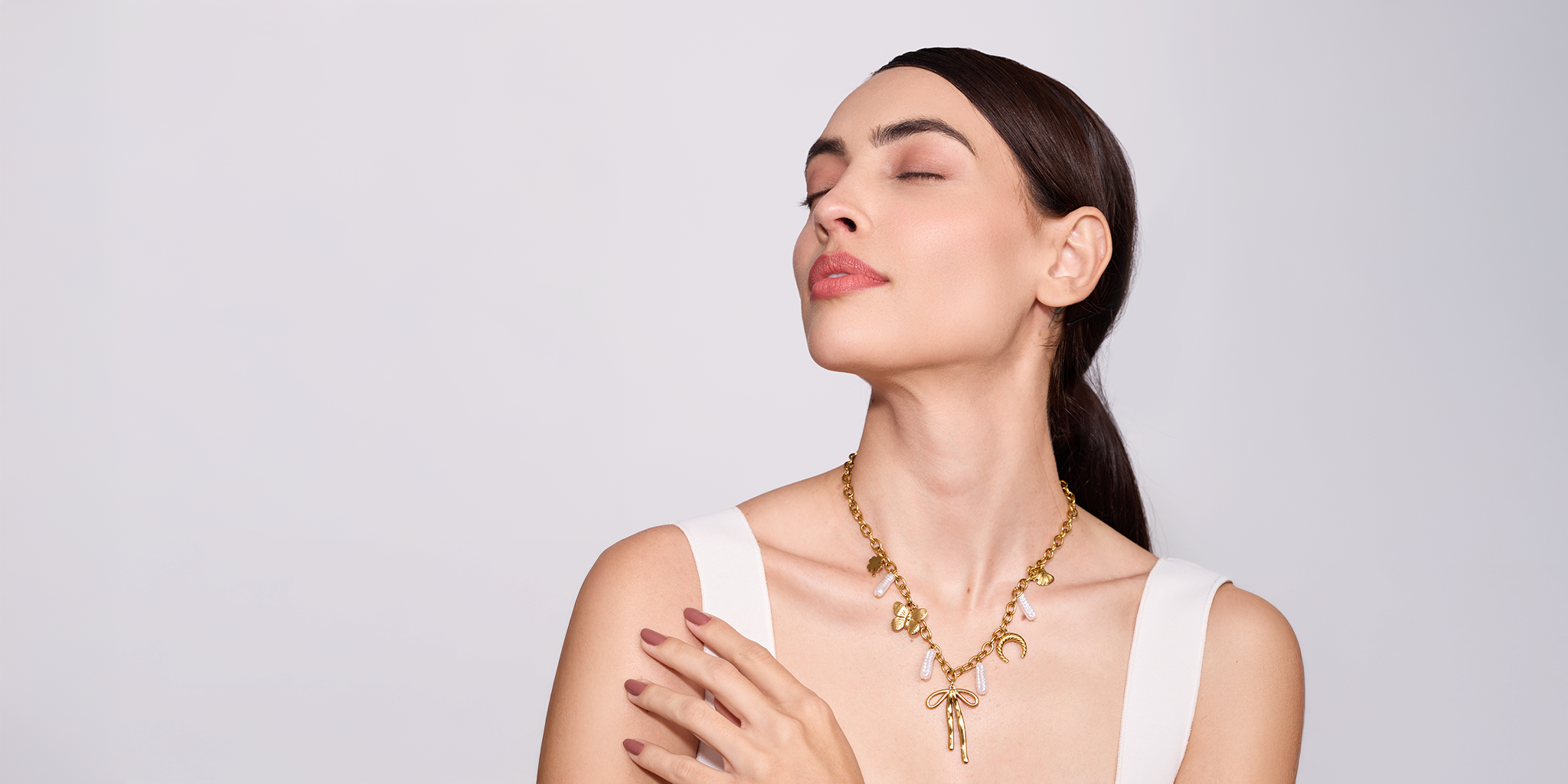 Woman wearing a gold necklace against a plain background