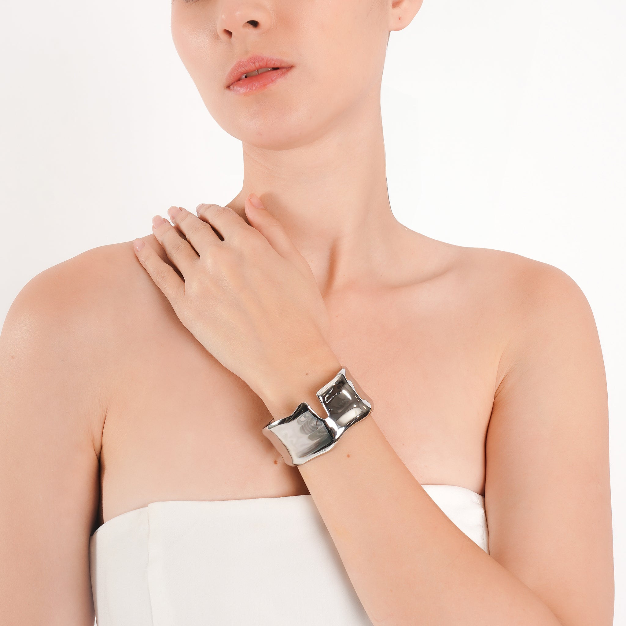 Model wearing an silver plated open cuff bracelet with a fluid, high-shine design, styled against a white outfit for a refined, elegant look.